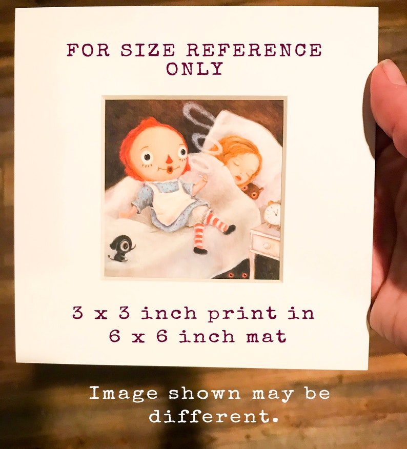 May include: A 3x3 inch print of a red-haired doll sitting on a bed with a sleeping girl. The print is matted in a 6x6 inch frame. The image is for size reference only.