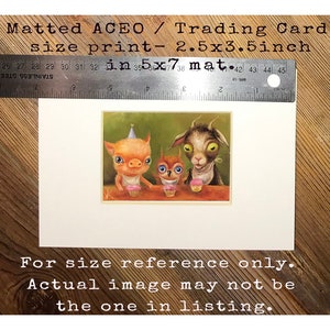 May include: A matted print of a whimsical illustration featuring a pig, an owl, and a goat wearing party hats and holding cupcakes. The print is 2.5 inches by 3.5 inches and is matted to a size of 3.5 inches by 7 inches. The text "For size reference only. Actual image may not be the one in listing." is printed below the illustration.