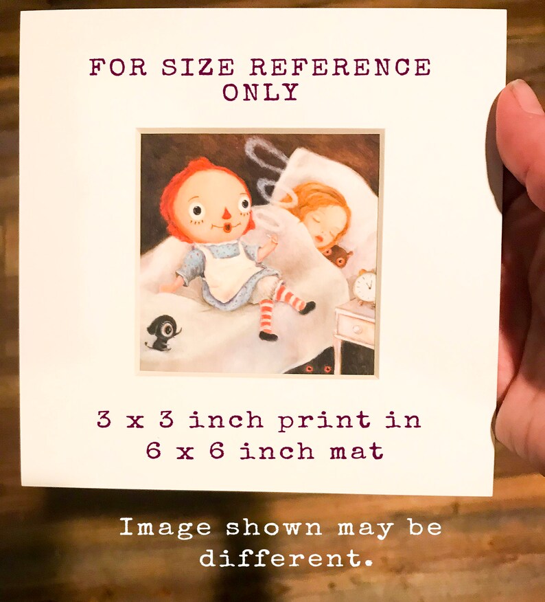 May include: A 3x3 inch print of a red-haired doll sitting on a bed with a girl sleeping next to her. The print is matted in a 6x6 inch mat. The image shown may be different.
