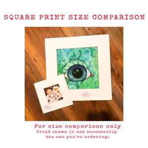 May include: Two square prints of artwork, one with a blue eye and green background, the other with a cartoon image. The larger print is matted to 12x12 inches, the smaller print is matted to 6x6 inches. "For size comparison only. Print shown is not necessarily the one you're ordering."
