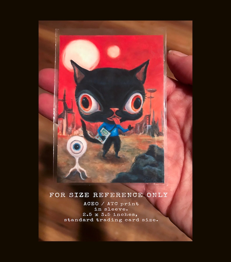 May include: A black cat with large eyes and a blue shirt stands on a red and brown landscape with a single eye creature in the foreground. The image is a 2.5 x 3.5 inch ATC print in a sleeve. FOR SIZE REFERENCE ONLY.
