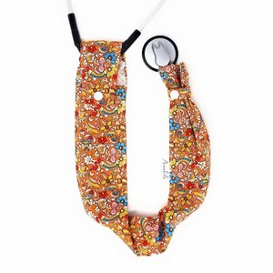 May include: A stethoscope holder with a floral pattern in shades of orange, yellow, blue, and pink. The holder has a white button and is made of fabric.
