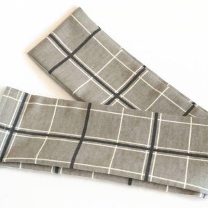May include: A gray and white plaid fabric with black stripes. The fabric is folded in half and the edges are visible.