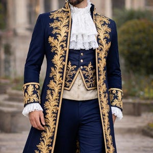 K&ouml;nnte beinhalten: Ein marineblauer Anzug mit goldener Stickerei. Der Anzug besteht aus einem langen Mantel, einer Weste und einer Hose. Der Mantel hat verzierte goldene Blattmuster an den R&auml;ndern und Manschetten. Ein wei&szlig;es R&uuml;schenhemd ist sichtbar.