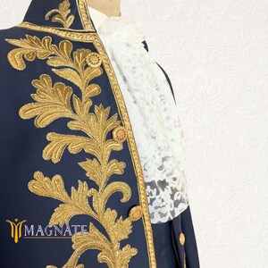 K&ouml;nnte beinhalten: Marineblaue Jacke mit aufwendiger goldener Stickerei und Holzkn&ouml;pfen. Die Jacke hat einen hohen Kragen und wird mit einem wei&szlig;en Spitzenjabot getragen. Das Wort "MAGNATE" ist in goldenen Buchstaben zu sehen.