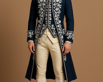 Könnte beinhalten: Ein marineblauer Mantel mit weißen Blumenstickereien, kombiniert mit einer cremefarbenen Weste und Kniebundhose. Der Mantel hat einen hohen Kragen und lange Ärmel mit bestickten Manschetten. Schwarze Schuhe vervollständigen das Ensemble.