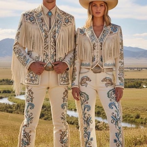 May include: Matching cream-colored cowboy outfits with intricate embroidery and fringe. The outfits include jackets, vests, and pants, paired with cowboy hats and boots. The embroidery features floral and horse motifs, with accents of blue and gold.