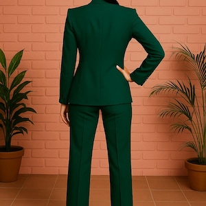 Puede incluir: Un traje de pantal&oacute;n verde oscuro, que incluye una blazer entallada con solapas y pantalones rectos a juego. El conjunto se combina con tacones color nude. El fondo presenta plantas en macetas y una pared con efecto ladrillo.