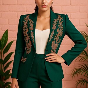 Puede incluir: Traje verde esmeralda con blazer y pantal&oacute;n a juego, con intrincados bordados dorados en las solapas. El traje a medida presenta un cierre de un solo bot&oacute;n y una parte superior blanca debajo. El conjunto est&aacute; sobre una pared de ladrillos rosas.