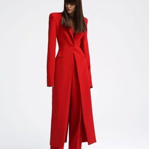 Può includere: Un vivace completo rosso con un blazer lungo con spalle strutturate e pantaloni a gamba larga abbinati. L'ensemble su misura è un outfit monocromatico, che mostra un'estetica elegante e moderna. Il design del completo è minimalista ed elegante.