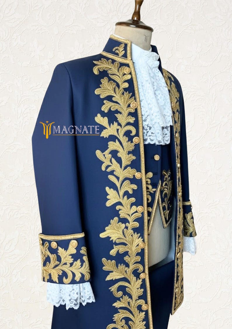 K&ouml;nnte beinhalten: Ein marineblauer formeller Anzug mit goldener Blumenstickerei. Der Anzug umfasst einen langen Mantel, eine Weste und wei&szlig;e Spitzentrimm. Der Mantel hat goldene Kn&ouml;pfe und aufwendige Details. Das Logo "MAGNATE" ist sichtbar.