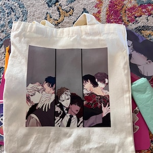 Könnte beinhalten: Eine weiße Canvas-Tragetasche mit einem aufgedruckten Bild von vier Männern aus einem Manga oder Anime. Die Männer sind in einem realistischen Stil gezeichnet und tragen verschiedene Outfits. Das Bild ist in drei Abschnitte unterteilt, wobei jeder Abschnitt ein anderes Männerpaar zeigt.