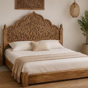 May include: A wooden bed frame featuring a tall, arched headboard with intricate floral carvings. The bed is dressed in white bedding, including two large pillows and a smaller rectangular accent pillow, topped with a beige textured throw blanket.