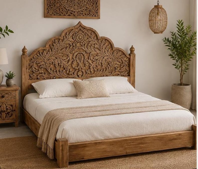 May include: A wooden bed frame featuring a tall, arched headboard with intricate floral carvings. The bed is dressed in white bedding, including two large pillows and a smaller rectangular accent pillow, topped with a beige textured throw blanket.