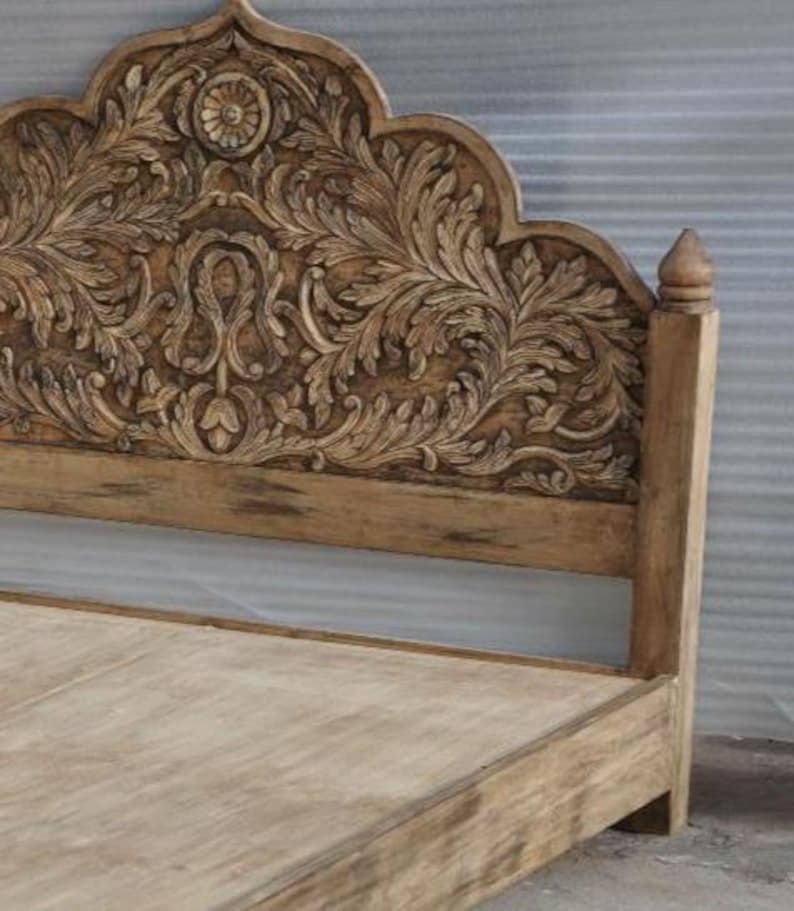 May include: A light brown wooden bed frame featuring an arched headboard with intricate, deep-relief floral and scroll carvings. The headboard is topped with a central circular medallion and features a smooth, flat wooden base frame.