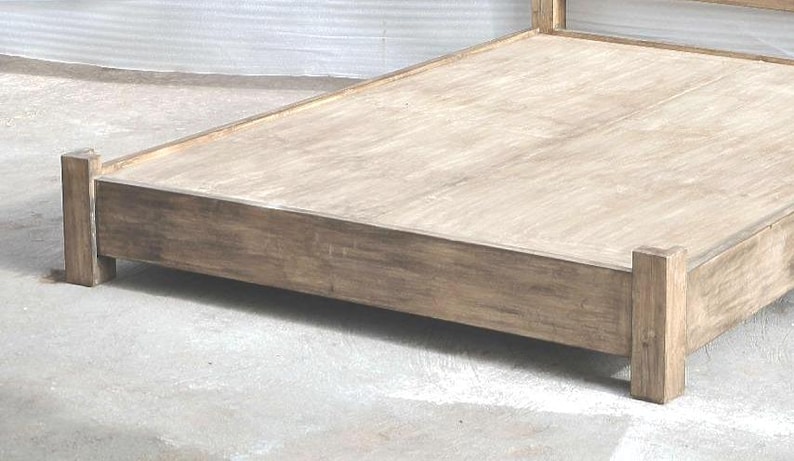 May include: A low-profile bed frame constructed from light brown wood with a visible grain pattern. The frame features a rectangular base with four sturdy corner posts and a flat platform surface designed to support a mattress without a box spring.