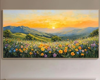 Op de afbeelding: Een landschapsschilderij toont een zonsondergang boven groene heuvels en een veld met kleurrijke wilde bloemen. Het kunstwerk, in een gouden lijst, hangt boven een open haard met een brandend vuur. De scène creëert een warme sfeer.