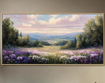 Puede incluir: Un cuadro de paisaje rectangular con un marco dorado fino que muestra un campo de flores silvestres moradas y blancas en primer plano, flanqueado por densos árboles verdes, con colinas y un cielo nublado en tonos rosa y azul.