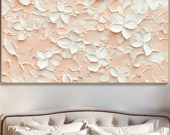 May include: A rectangular canvas art piece featuring a textured floral design. The artwork showcases white flowers against a soft peach background. The flowers have a raised, three-dimensional appearance, creating a tactile effect. The piece is framed in a gold-colored border.