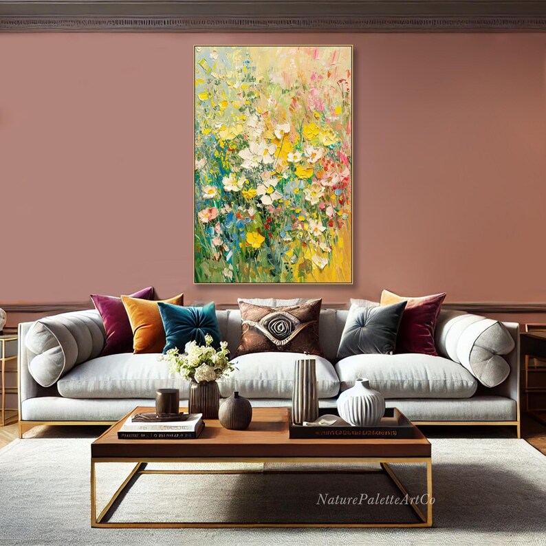 May include: An abstract floral painting in a gold frame hangs above a grey sofa with colourful throw cushions. The artwork features a vibrant mix of yellow, white, and pink flowers. A wooden coffee table with decorative items sits in front of the sofa.