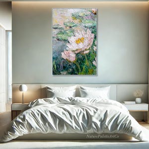 May include: A framed oil painting of water lilies in a bedroom setting. The artwork features white and pink flowers with yellow centers, surrounded by green lily pads. The painting is displayed above a bed with white bedding.