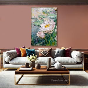 May include: An oil painting of white and pink water lilies with yellow centers, set against a backdrop of green lily pads and water. The artwork is displayed above a gray sofa with colorful throw pillows, a wooden coffee table, and a rug.