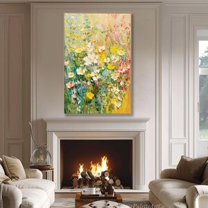 May include: An abstract floral painting in a gold frame. The artwork depicts a vibrant array of yellow, white, pink, and blue flowers. The painting is displayed above a fireplace in a living room.