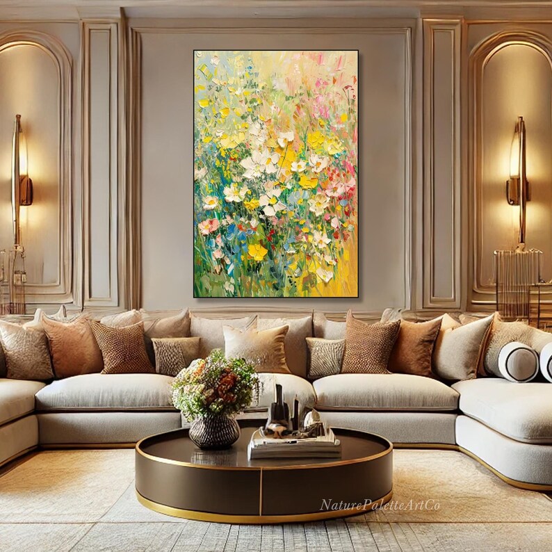 May include: An abstract floral painting featuring yellow, white, pink, and green flowers. The artwork hangs above a beige sofa with cushions. A round coffee table and wall lights are also visible in the room.