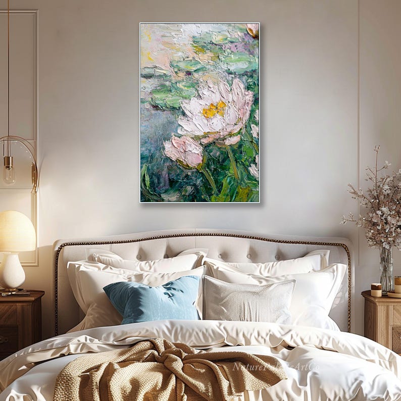 May include: A framed oil painting of white and yellow water lilies with green lily pads. The artwork has a textured, impressionistic style. The painting is displayed above a bed with white bedding and a blue pillow.