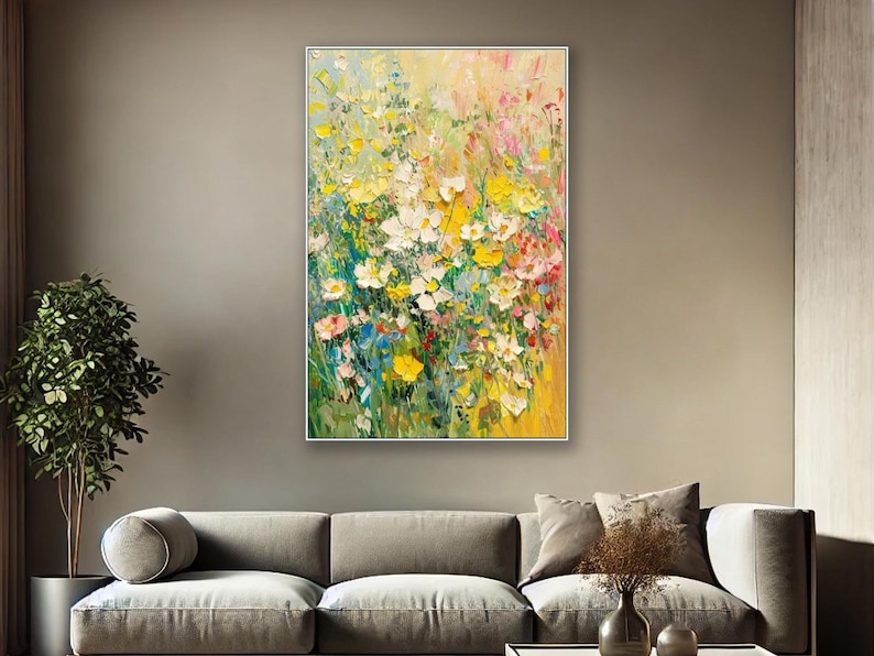 May include: An abstract floral painting featuring yellow, white, pink, and blue flowers. The artwork is framed in a silver border and hangs on a neutral wall, above a grey sofa.