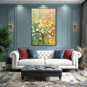 May include: An abstract floral painting in a black frame. The artwork showcases a vibrant array of yellow, white, pink, and green flowers. The painting is displayed above a white sofa with red and blue cushions, creating a colourful living room setting.