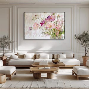 May include: A large abstract painting of pink and white flowers in a vase. The painting is hanging on a white wall in a living room setting with a white sofa and a wooden coffee table.