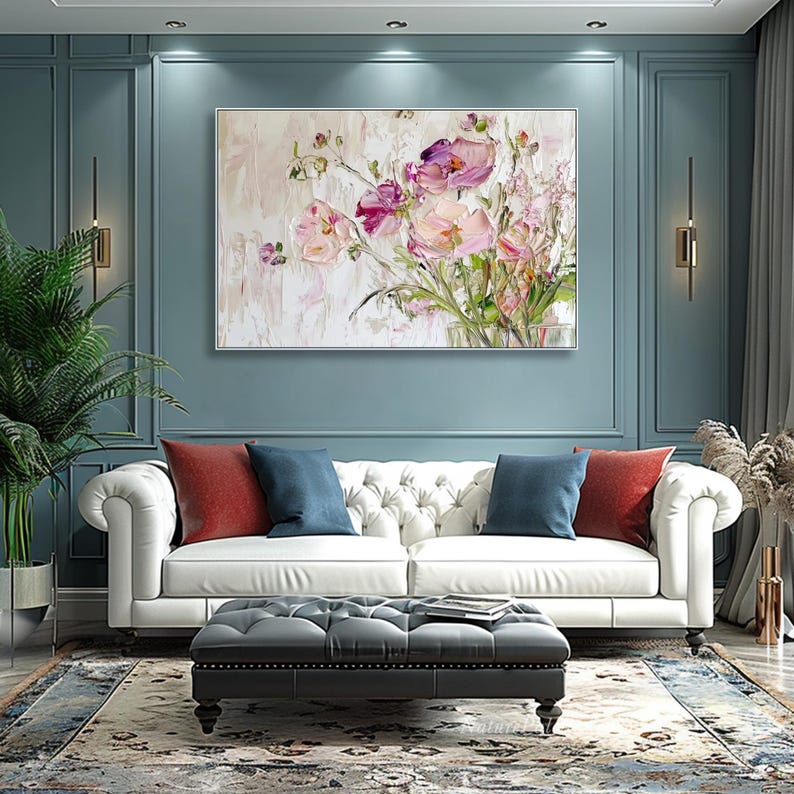 May include: A white sofa with red and blue pillows in a room with a large painting of pink flowers on a blue wall.