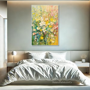 May include: An abstract floral painting in a white frame. The artwork features a vibrant mix of yellow, white, pink, and green flowers. The painting is displayed above a bed with white bedding. The artist's name, NaturePaletteArtCo, is visible.