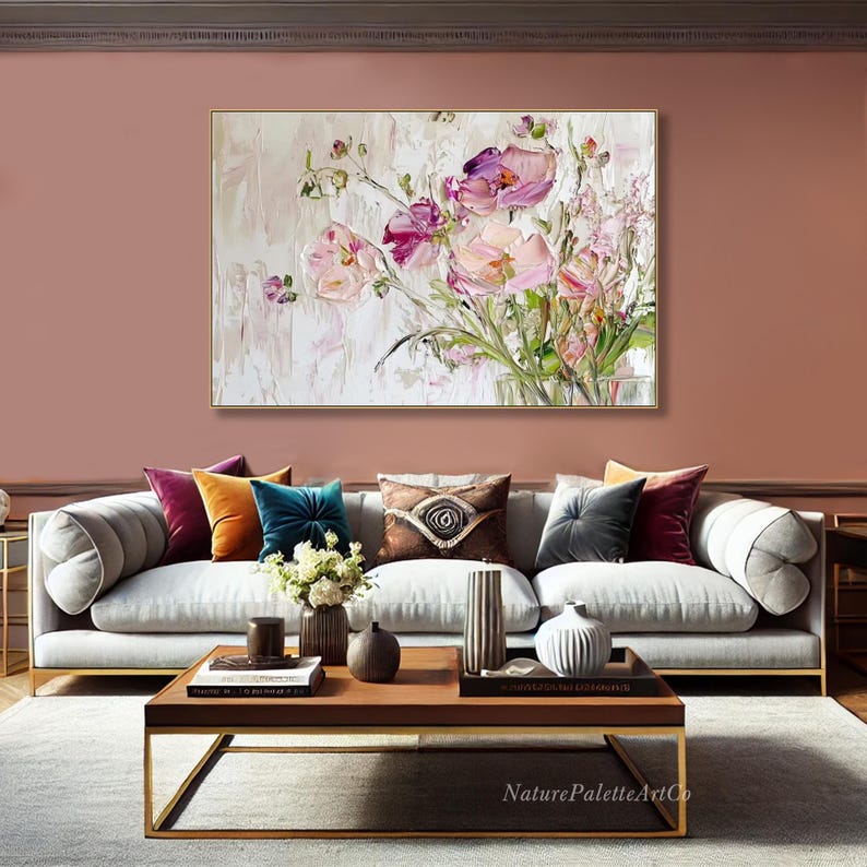 May include: A large abstract painting of pink and purple flowers on a white background. The painting is hanging on a wall in a living room with a white sofa and gold coffee table.