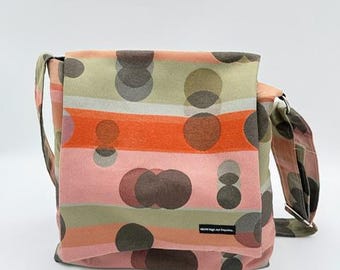 May include: A shoulder bag with a flap closure. The bag features a repeating pattern of horizontal stripes in shades of pink, orange, and green, overlaid with brown and gray circles. The bag has a long strap and a small label with text.