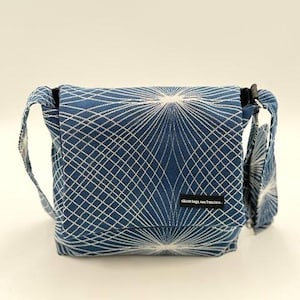 May include: A blue crossbody bag with a white geometric pattern. The bag has a flap closure and a shoulder strap. The bag has a small black tag that reads "skinte bags, san francisco."