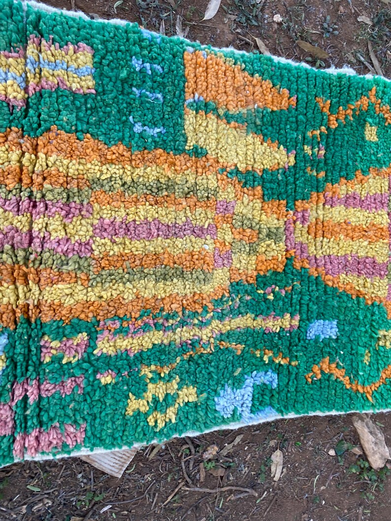 May include: A colorful, textured rug with a vibrant design. The rug features a mix of green, orange, yellow, pink, and blue hues. The rug's design includes geometric and abstract patterns, creating a visually appealing textile.