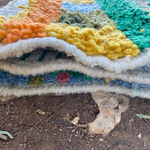 May include: A colorful, handmade rug with a geometric design. The rug features a variety of colors, including orange, yellow, green, and blue. The rug is made of a thick, textured material, and the edges are finished with a white border. The rug is folded over.