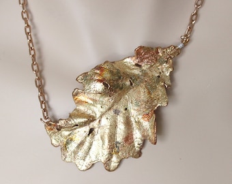 May include: A gold-colored leaf pendant necklace. The pendant is a detailed, textured leaf shape with a metallic finish. The chain is a matching gold color, creating a cohesive and elegant piece of jewelry.