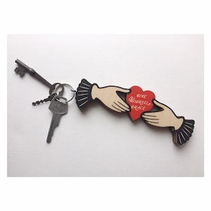 May include: Wooden keychain with two hands holding a red heart with the text "Give Yourself Grace".