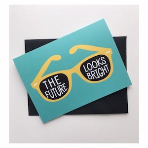 May include: A turquoise card with a yellow pair of sunglasses. The sunglasses have the text "The Future" on the left lens and "Looks Bright" on the right lens.