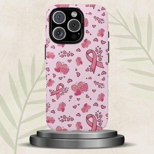 May include: Pink phone case with a pattern of pink ribbons, hearts, and butterflies. The case features a pink ribbon, a symbol of breast cancer awareness. The design includes various heart shapes and butterfly patterns.