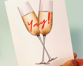 May include: A white card with two champagne flutes filled with a golden liquid. The word "yay!" is written in red cursive.