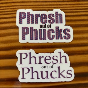 May include: Two white stickers with the text "Phresh out of Phucks" in black and purple lettering. The top sticker has a purple background with a repeating pattern of red donuts.
