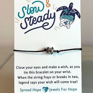 May include: A black string bracelet with a silver turtle charm. The card reads "Slow & Steady" with a turtle illustration and "Spread Hope Jewels For Hope Gifts That Give Back www.jewelsforhope.etsy.com".