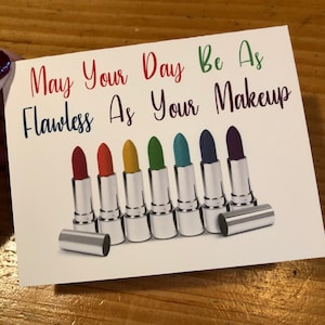 May include: A card with the text "May your day be as flawless as your makeup" and a row of eight silver lipstick tubes with colorful lipstick inside.