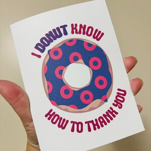 May include: A white greeting card with a donut design. The donut has a blue center with pink circles and a brown outline. The card reads "I DONUT KNOW HOW TO THANK YOU" in pink text.