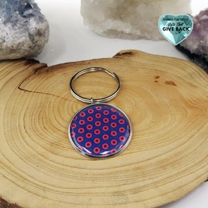 May include: A silver key chain with a round blue and pink donut pattern charm. The charm has a silver border. The key chain is on a wooden surface.