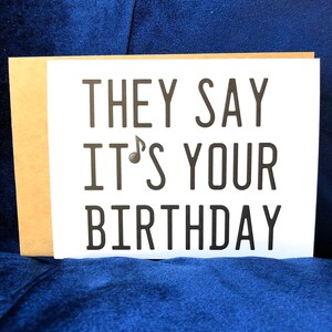 May include: A white card with black text that reads "They say it's your birthday". The card is sitting on a blue surface.